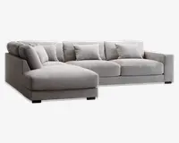 Moderne hjørnesofa i lysegråt stof med venstrevendt chaiselong. Sofaen har brede, firkantede armlæn, dybe sædehynder og fem matchende ryghynder for ekstra komfort. Betrækket har en diskret tekstureret vævning, og sofaen står på lave, sorte blokformede ben.