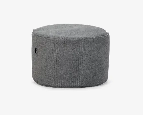 Rund, blød puf med et glat, strikket betræk i grå farve. Overfladen ser polstret og behagelig ud, velegnet som siddeplads eller fodskammel. Syningerne er diskrete, og designet er minimalistisk, hvilket gør den alsidig til forskellige indretninger. Et lille stofmærke ses på siden.