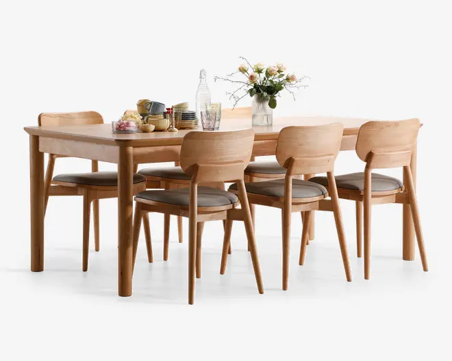 Rektangulært spisebordssæt i lyst træ med seks matchende stole, der har buede rygge og polstrede grå sædehynder. Bordet er dækket med tallerkener, kopper, en tekande og en vase med friske blomster, hvilket skaber en indbydende og elegant spiseoplevelse. Designet er moderne og minimalistisk med glatte kanter og solide ben.