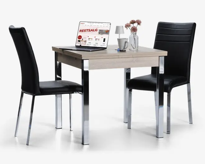 Et kompakt spisebordssæt med et firkantet bord i lys træfinish og kromben, samt to sorte stole i kunstlæder med høje rygge og vandrette syninger. Bordet er dekoreret med en bærbar computer, en hvid kop, en lille vase med lyserøde blomster og et glas vand, hvilket viser, at sættet egner sig både til spisning og arbejde.