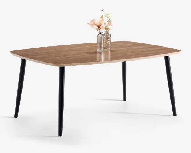 Rektangulært bord med en glat bordplade i lyst trælook og fire let skråtstillede sorte metalben. På bordpladen står to glasvaser; den ene indeholder en stor kunstig blomst i lyserød nuance, og den anden har en lille buket med hvide og lyserøde blomster. Bordet har et minimalistisk, moderne design, der egner sig til spise- eller arbejdsbrug.