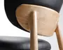 Nærbillede af en stol med en glat, lys træramme med afrundede kanter. Ryglæn og sæde er polstret med sort læder eller læderlignende materiale, hvilket giver et elegant og moderne udseende. Træets årer er synlige og fremhæver den naturlige finish, og konstruktionen virker robust med sømløse samlinger mellem ben og ryglænets støtte.