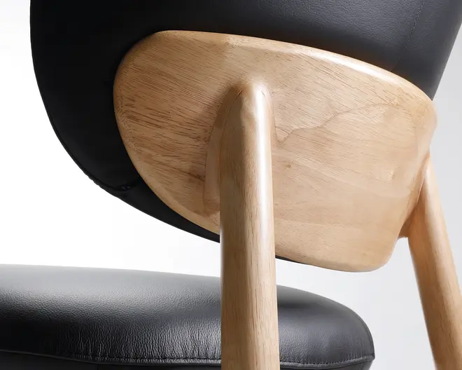 Nærbillede af en stol med en glat, lys træramme med afrundede kanter. Ryglæn og sæde er polstret med sort læder eller læderlignende materiale, hvilket giver et elegant og moderne udseende. Træets årer er synlige og fremhæver den naturlige finish, og konstruktionen virker robust med sømløse samlinger mellem ben og ryglænets støtte.