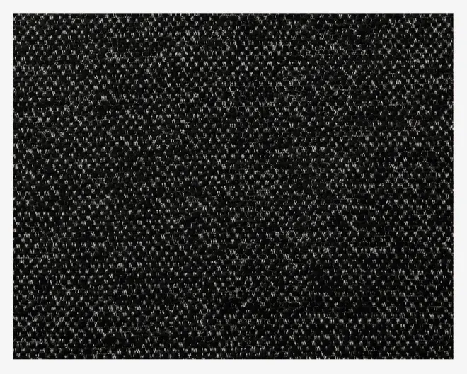 Nærbillede af et tekstiler med tæt, løkket overflade. Materialet er overvejende sort med små, jævnt fordelte lysegrå nister, hvilket giver et diskret, spættet mønster. Overfladen ser slidstærk ud og egner sig til områder med meget trafik.