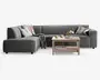 En moderne L-formet hjørnesofa betrukket med mørkegråt stof, med brede armlæn og bløde sædehynder. Sofaen er pyntet med forskellige dekorative puder i neutrale og stribede mønstre samt et hyggeligt tæppe, der er lagt over den ene side. Foran sofaen står et sofabord i lyst træ med en underhylde, hvor der ligger magasiner, og på bordpladen er der krus, en tallerken og en vase med blomster, hvilket skaber en indbydende og komfortabel stueatmosfære.