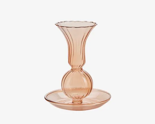 Elegant glasvase i en blød rosa farve med bølget, udadbuet kant og en rund, kugleformet midte. Vasens fod står på en matchende rund tallerken, begge med en glat og blank overflade. Lodrette linjer fremhæver vasens kurver og giver et sofistikeret udtryk.