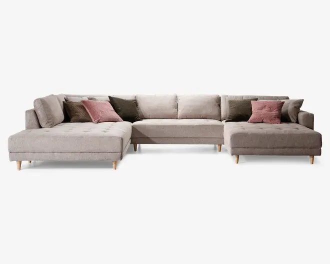 Stor L-formet sofa med lyse beige betræk og ben i træ. Sofaen har knapdetaljer på sædehynderne og leveres med flere pyntepuder i afdæmpede rosa og olivengrønne nuancer for ekstra komfort og stil. Sofaen har lav ryg og brede siddepladser, velegnet til rummelige stuer.