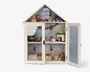 Et miniature vitrineskab formet som et hus med to glasdøre, dekoreret til jul. Indvendigt er der tre hylder med små møbler og festlige tilbehør, herunder en grøn lænestol, en pejs med julestrømper, en guirlande med lys, et lille køkkenområde og forskellige julepynt som en bamse, en slæde og indpakkede gaver. Baggrunden har snefnug og juletræer, hvilket understreger det hyggelige juletema.