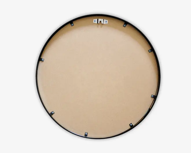 Billedet viser bagsiden af et rundt objekt med en glat, lysebrun overflade, sandsynligvis lavet af MDF eller lignende materiale. Der er en sort cirkulær ramme langs kanten og flere små metalclips jævnt fordelt rundt om kanten til fastgørelse af bagstykket. Øverst i midten er der et metalophæng til vægmontering.