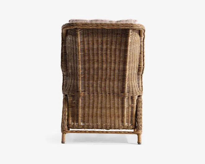 Billedet viser et møbel med en tæt flettet ramme af rattan eller flet. Ryglænet er let buet og forstærket med ekstra flet for øget holdbarhed. Benene er korte og solide, og den samlede finish har en naturlig, lys brun farve, der fremhæver materialets tekstur. Øverst ses en kant med en pude eller polstring, hvilket indikerer ekstra komfort.