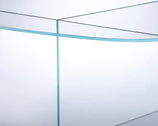 Nærbillede af en transparent glasplade med polerede kanter, der viser materialets tykkelse og klarhed. Glasset har en let blågrøn nuance langs kanterne, hvilket indikerer høj kvalitet. Pladerne er samlet i en ret vinkel, hvilket viser præcist håndværk og sømløse samlinger.