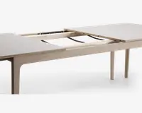 Rektangulært bord med lys træramme og ben, vist i udtrukket position med bordpladen delt i midten, så udtræksmekanismen er synlig. Bordpladen har en glat, lys overflade, og udtrækssystemet bruger skinner, der gør det muligt at indsætte ekstra plader og dermed forlænge bordet til flere siddepladser.