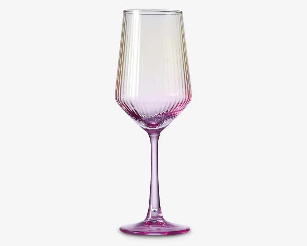 Elegant glas med høj, slank stilk og fløjteformet skål. Glasset har en diskret farveovergang, der går fra klart øverst til en livlig pink nuance ved bunden. Lodrette riller giver både et dekorativt udtryk og bedre greb. Bunden er bred og stabil, også farvet pink, hvilket fuldender det samlede design.