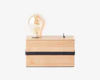 Rektangulær lampe med en base af lyst naturtræ, udstyret med en synlig Edison-pære i vintage-stil med synlig glødetråd. Lampen har en sort, vandret metalstribe med to skruer på forsiden og en lille sølvfarvet vippekontakt på toppen til betjening.