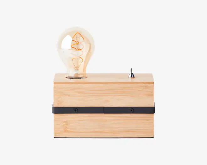 Rektangulær lampe med en base af lyst naturtræ, udstyret med en synlig Edison-pære i vintage-stil med synlig glødetråd. Lampen har en sort, vandret metalstribe med to skruer på forsiden og en lille sølvfarvet vippekontakt på toppen til betjening.