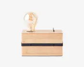 Rektangulær lampe med en base af lyst naturtræ, udstyret med en synlig Edison-pære i vintage-stil med synlig glødetråd. Lampen har en sort, vandret metalstribe med to skruer på forsiden og en lille sølvfarvet vippekontakt på toppen til betjening.