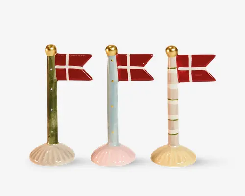 Tre dekorative flagstænger, hver med et rødt og hvidt flag med kors. Flagstængerne har forskellige designs: én er grøn med guldfarvede prikker, én er lyseblå med guldfarvede prikker, og én er hvid med lyserøde striber og grønne ringe. Hver stang har en guldfarvet kugle på toppen og står på en muslingeformet fod i matchende pastelfarver.