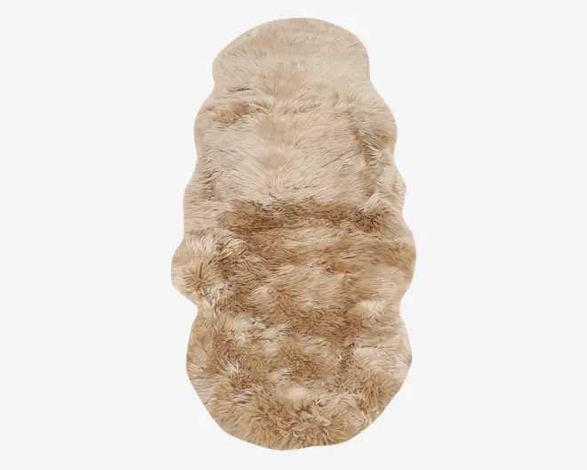 Et langt, blødt fåreskindstæppe i beige med naturlig, ujævn form og tyk, blød pels. Overfladen har en let bølget struktur og en blanding af lyse og mørkere beige nuancer, hvilket giver et hyggeligt og luksuriøst udtryk.