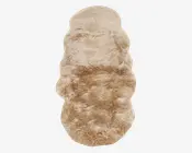 Et langt, blødt fåreskindstæppe i beige med naturlig, ujævn form og tyk, blød pels. Overfladen har en let bølget struktur og en blanding af lyse og mørkere beige nuancer, hvilket giver et hyggeligt og luksuriøst udtryk.