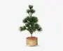 Kunstig plante med tæt, spidst grønt løv arrangeret i runde klynger på flere grene. Planten står i en cylindrisk potte med en naturlig træ-lignende overflade og er dækket med rødbrunt dekorativt muld. Udtrykket er frodigt og velordnet, velegnet til indendørs dekoration.