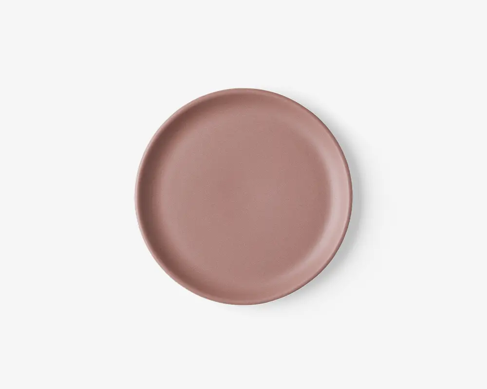 En rund, flad tallerken med en glat, mat overflade i en afdæmpet støvet rosa farve. Tallerkenen har en let hævet kant og et minimalistisk, moderne design uden mønstre eller dekorationer.