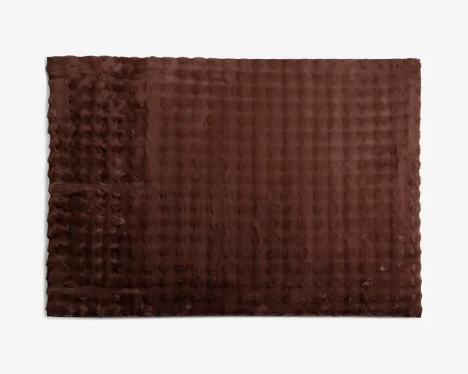 Et rektangulært, mørkebrunt tekstil med en vaffellignende, struktureret overflade. Materialet har et mønster af hævede firkanter, hvilket giver det et blødt og hyggeligt udseende. Kanterne er pænt afsluttede, og stoffet ser tykt og blødt ud, velegnet til varme og komfort.