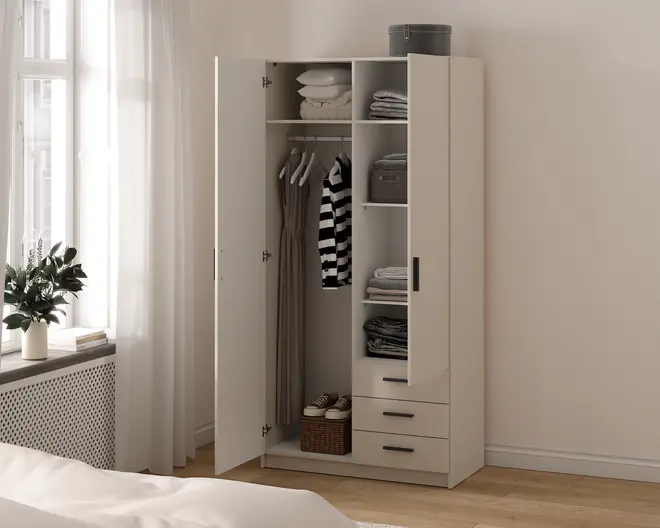 Et fritstående garderobeskab med et minimalistisk design i en lys beige farve. Skabet har to låger, hvoraf den ene er åben og viser indretningen indeni. Indvendigt er der en bøjlestang med tøj på bøjler, flere hylder med sammenfoldet tøj, opbevaringskasser og en kurv nederst. Skabet har også tre skuffer med slanke sorte greb for ekstra opbevaringsplads. Udtrykket er rent og moderne, velegnet til et nutidigt soveværelse.