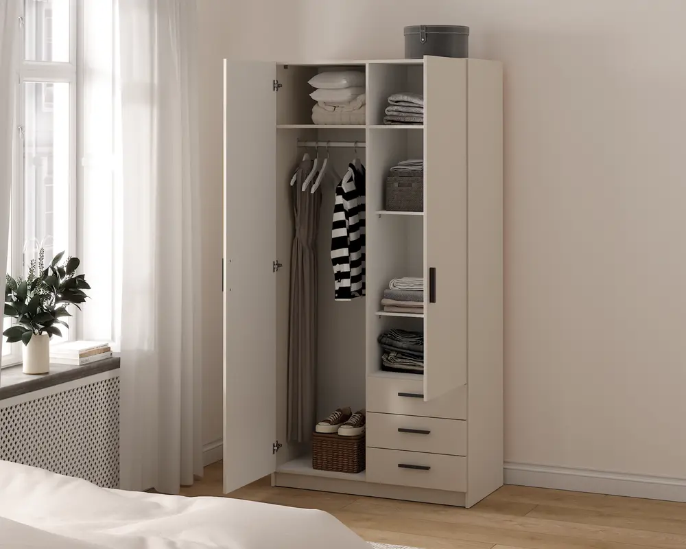 Et fritstående garderobeskab med et minimalistisk design i en lys beige farve. Skabet har to låger, hvoraf den ene er åben og viser indretningen indeni. Indvendigt er der en bøjlestang med tøj på bøjler, flere hylder med sammenfoldet tøj, opbevaringskasser og en kurv nederst. Skabet har også tre skuffer med slanke sorte greb for ekstra opbevaringsplads. Udtrykket er rent og moderne, velegnet til et nutidigt soveværelse.