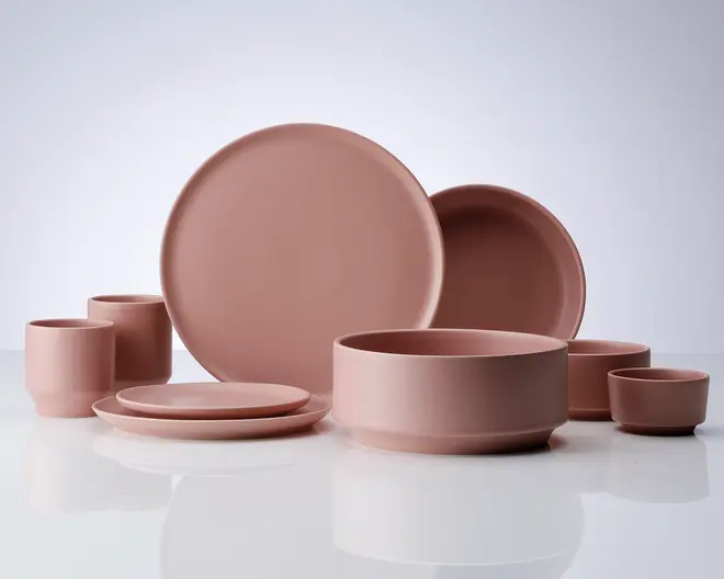 Et sæt mat, lyserødt keramikservice med forskellige dele, herunder store og små tallerkener, skåle i flere størrelser og kopper. Designet er minimalistisk med glatte overflader og rene, afrundede kanter, hvilket giver et moderne og elegant udtryk. Delene er ensfarvede og har en blød, afdæmpet finish.