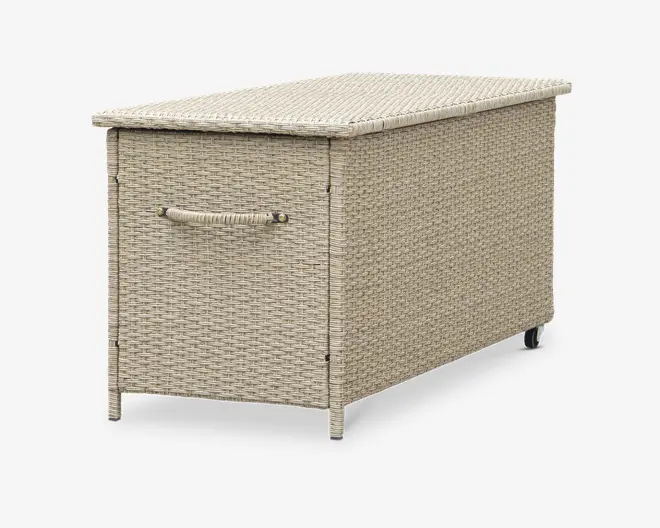Rektangulær opbevaringsboks med flettet rattan-lignende ydre i en lys beige farve. Boksen har et hængslet låg for nem adgang, et solidt håndtag på den ene side for nem transport samt små hjul i bunden for let bevægelse. Designet er vejrbestandigt og egner sig til udendørs brug.