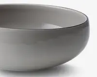 Et nærbillede af en glat, rund skål med en blank, lysegrå overflade. Skålen har et enkelt, minimalistisk design med blødt buede sider og en let tyk kant. Både indersiden og ydersiden har samme farve, hvilket giver et moderne og elegant udtryk.