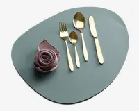 Et sæt med fire guldfarvede bestikdele, herunder en gaffel, en lille ske, en stor ske og en kniv, arrangeret pænt på en mat, uregelmæssigt formet lyseblå dækkeserviet. Ved siden af bestikket ligger en støvet rosa stofserviet foldet som en rose, hvilket giver et elegant udtryk.
