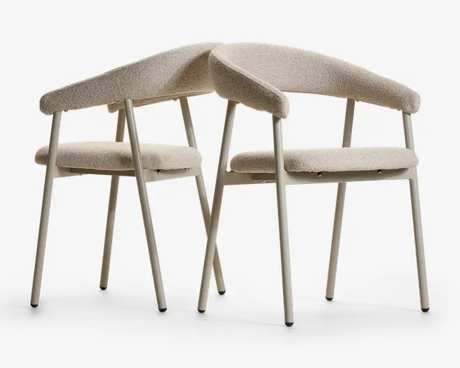To matchende polstrede stole med beige stofsæder og -rygge, slanke lyse koniske ben og buede polstrede ryglæn, der giver et moderne, skulpturelt udtryk.