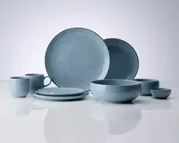 Et sæt keramikservice i en blød mat blå finish, bestående af to store middagstallerkener, to mindre sidetallerkener, to krus med hank, en stor serveringsskål, en mellemstor skål og en lille dip-skål. Delene har en glat, let afrundet form og en ensartet farve med et diskret blankt skær. Kanterne på tallerkener og skåle er blødt buede, og det samlede design er minimalistisk og moderne.