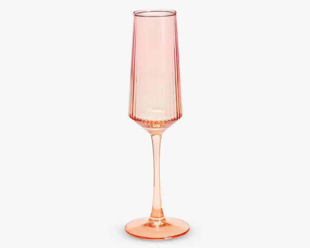 Et højt, slankt glas med fløjteform, lavet af gennemsigtigt glas med lyserødt skær. Glasset har en lang, elegant stilk og en bred, stabil fod. Skålen har diskrete lodrette riller, som giver tekstur og et visuelt interessant udtryk.