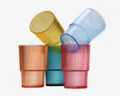 Sæt med fire stabelbare drikkeglas, hver i en forskellig gennemsigtig farve: orange, gul, blå og pink. Glassene har en lodret rillet struktur på ydersiden, hvilket giver dem et moderne og stilfuldt udseende. Glassets sider er lige med en let tyk bund for stabilitet.