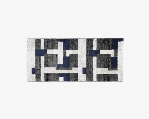 Rektangulært tæppe med et moderne geometrisk mønster af sammenlåsende blokke i sort, grå, hvid og mørkeblå. Designet er symmetrisk og markant, hvilket giver et moderne udtryk. Overfladen ser blød og luftig ud.