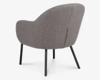 Billedet viser bagsiden af en moderne stol med rundet, buet ryglæn og armlæn. Stolen er polstret med et tekstureret, lysebrunt stof og har fire slanke, sorte metalben, der er let udadskrånende for stabilitet. Betrækket har en diskret lodret syning ned langs ryggen.