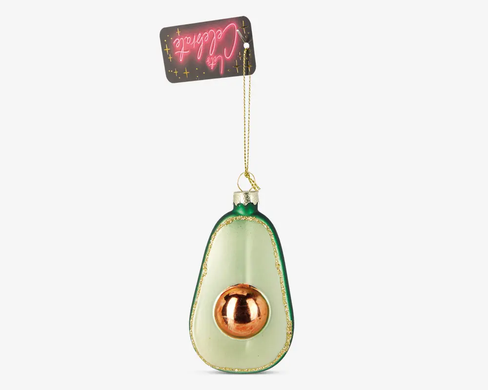 En dekorativ pynt formet som en halv avocado med en skinnende, metallisk gylden sten og glitrende grøn kant. Pynten hænger i et gyldent bånd og har et festligt mærke øverst.