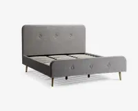En moderne sengeramme med et lysegråt polstret hovedgærde og fodgærde, begge med enkle knapdetaljer. Rammen har lameller af træ til madrasstøtte og står på skrå, træben, hvilket giver et udtryk i retrostil. Det samlede design er minimalistisk og stilrent, velegnet til moderne soveværelser.