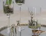 Klare dekorative glasgenstande arrangeret på et spejlfad, hver med et lille skovmotiv med mos, små sten og metalliske hjortefigurer i høje glas på stilk og en cylindrisk glasbeholder.