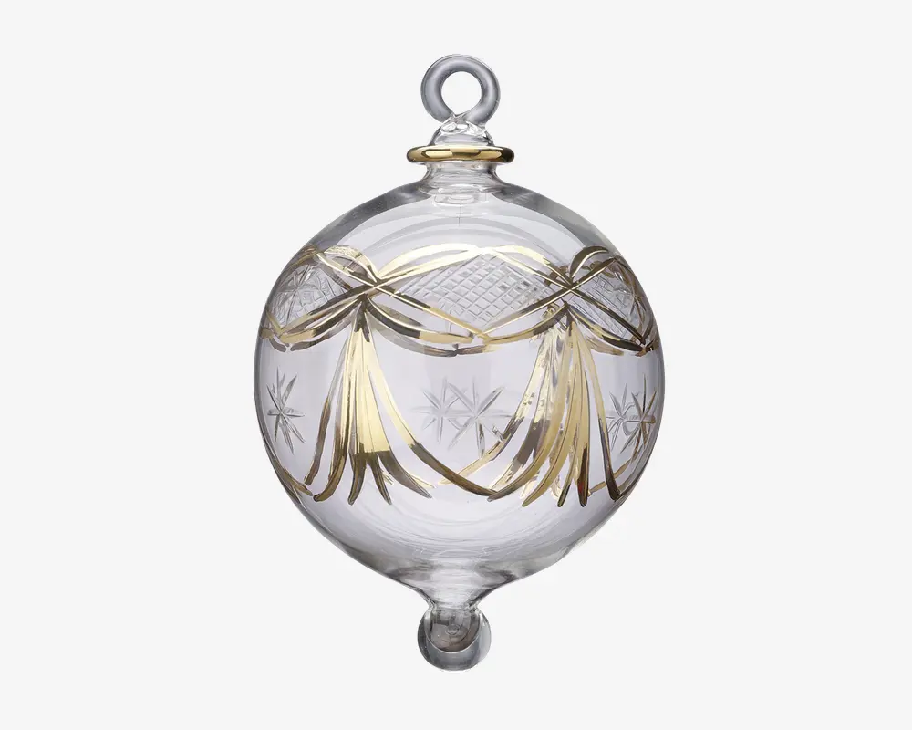 En kugleformet julekugle af klart glas med elegante guldfarvede båndlignende dekorationer og indgraverede stjernemønstre. Kuglen har en løkke øverst til ophængning og en lille rundet spids i bunden. Gulddetaljerne giver et festligt og luksuriøst udtryk til det gennemsigtige glas.