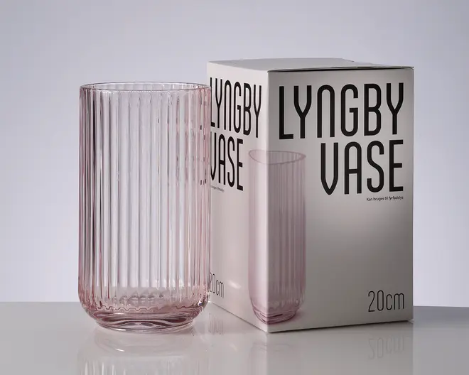 En høj, cylindrisk vase i ribbet glas med en lyserød tone, vist ved siden af sin matchende æske med teksten "LYNGBY VASE" og "20 cm".