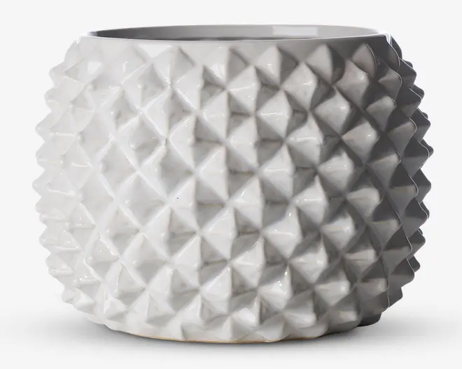 En rund, hvid keramisk beholder med blank overflade og et markant geometrisk mønster. Overfladen er dækket af gentagne, opadstående pyramideformede knopper, hvilket giver et moderne og taktilt udtryk. Åbningen foroven er bred, og formen er let tilspidset mod bunden.