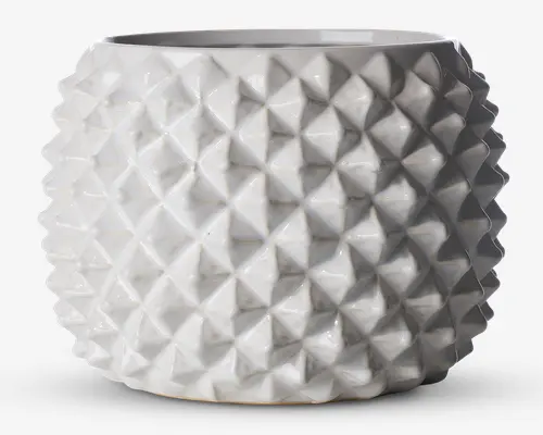 En rund, hvid keramisk beholder med blank overflade og et markant geometrisk mønster. Overfladen er dækket af gentagne, opadstående pyramideformede knopper, hvilket giver et moderne og taktilt udtryk. Åbningen foroven er bred, og formen er let tilspidset mod bunden.