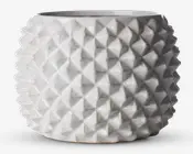 En rund, hvid keramisk beholder med blank overflade og et markant geometrisk mønster. Overfladen er dækket af gentagne, opadstående pyramideformede knopper, hvilket giver et moderne og taktilt udtryk. Åbningen foroven er bred, og formen er let tilspidset mod bunden.