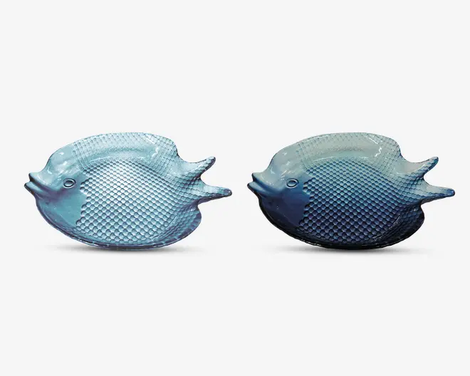 Sæt med to gennemsigtige blå glasfade formet som fisk, med detaljerede skæl og finner. Fadenes overflade er tekstureret på kroppen og har glatte kanter, hvor fiskens mund og øjne er tydeligt markeret. Designet er dekorativt og fantasifuldt, velegnet til servering af forretter eller som pyntegenstande.