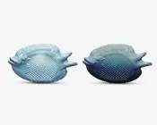 Sæt med to gennemsigtige blå glasfade formet som fisk, med detaljerede skæl og finner. Fadenes overflade er tekstureret på kroppen og har glatte kanter, hvor fiskens mund og øjne er tydeligt markeret. Designet er dekorativt og fantasifuldt, velegnet til servering af forretter eller som pyntegenstande.