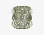 Et klart glasobjekt med cylindrisk form, der har en overflade med store, buede boblelignende forhøjninger arrangeret i et gittermønster. Glasset har en let iriserende finish, som reflekterer lyset og skaber diskrete regnbueeffekter på nogle af boblerne. Udseendet er moderne og dekorativt.