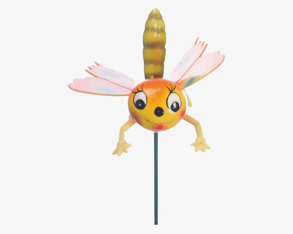 En fantasifuld havepynt formet som et tegneserieagtigt insekt med en rund gul-orange krop, store udtryksfulde øjne og et smilende ansigt. Den har to lyserøde vinger med røde detaljer, to gule arme med åbne hænder og en stribet gul og brun hale. Pynten er monteret på en tynd metalpind, så den let kan placeres i jorden.